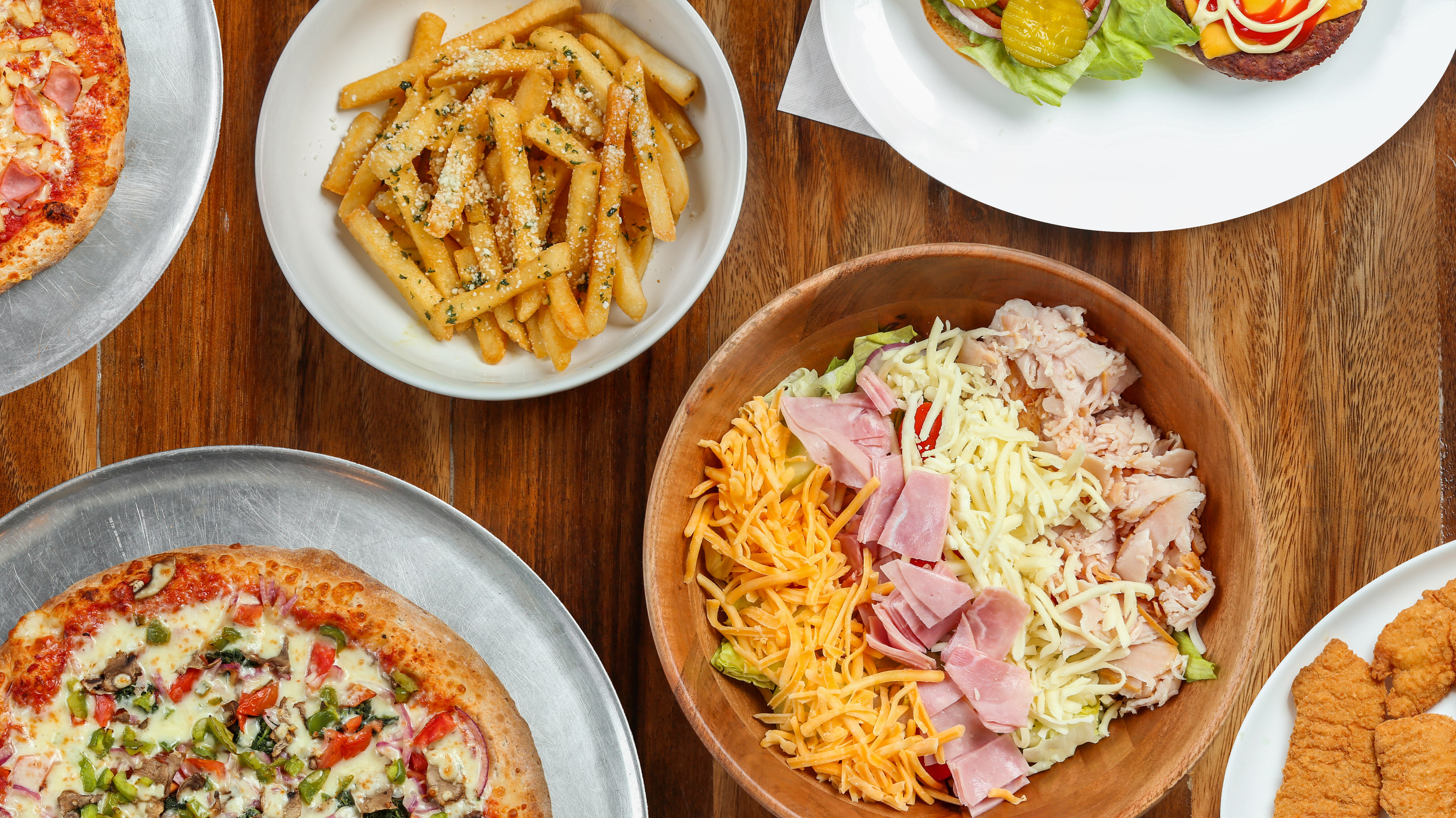 Spread of Pizza Perfectta dishes including specialty pizza, salad, garlic fries and chicken tenders